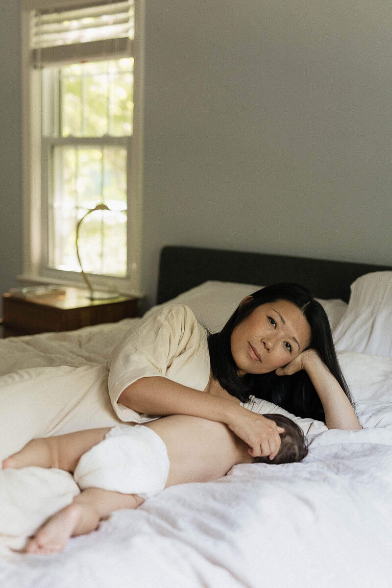 Mother nurses baby on bed during relaxed in-home lifestyle family photography session in Cleveland Heights.
