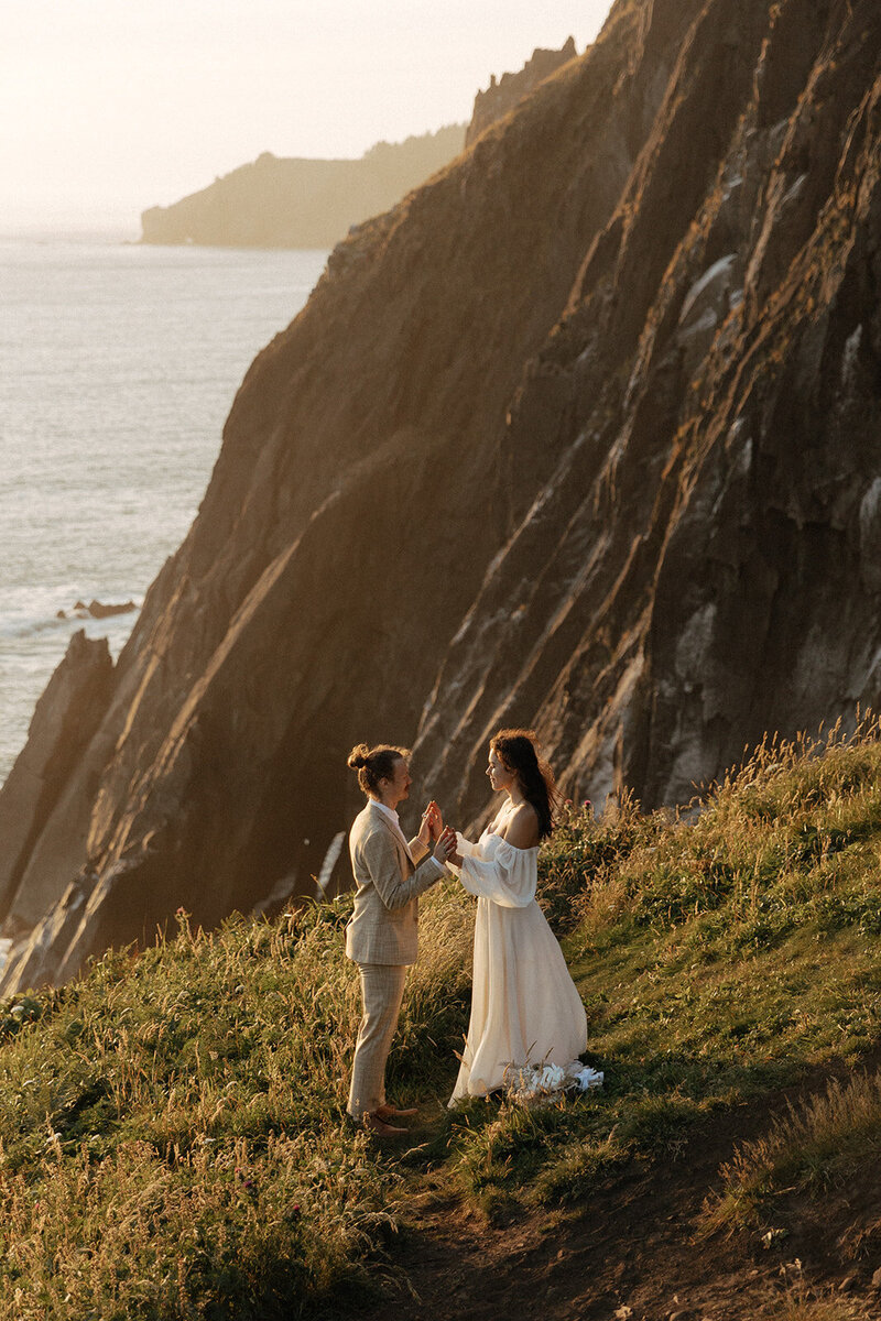 Couple exchanging vows on a seaside cliff at sunset during an international elopement.