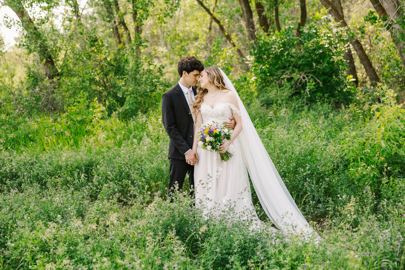 Bride and groom standing with their heads together in front of a wooded area