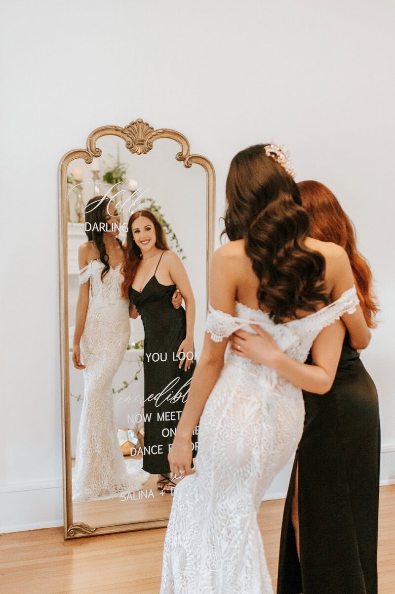 Bride and friend looking into a mirror with calligraphy message.