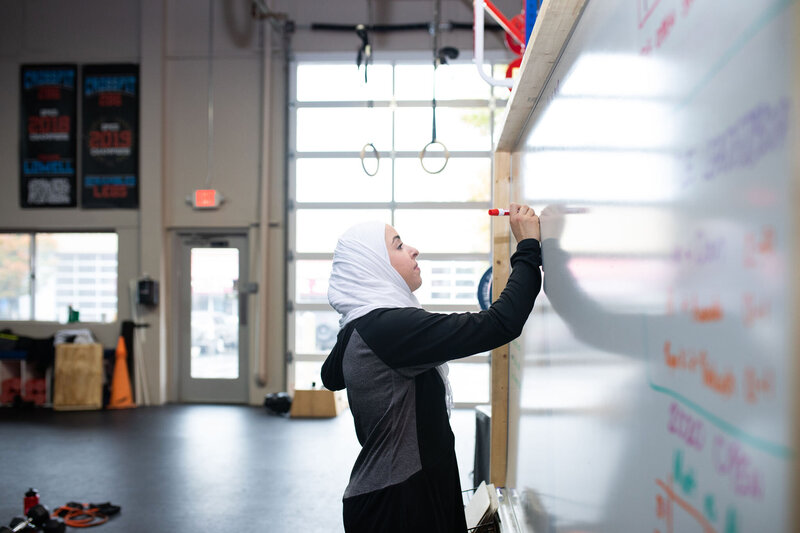 Fitness hijabi coach Hanan writing a workout plan in a gym  on a white board