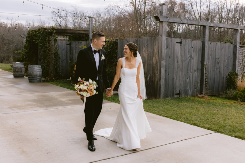 Couple walking in wedding attire smiling at each other