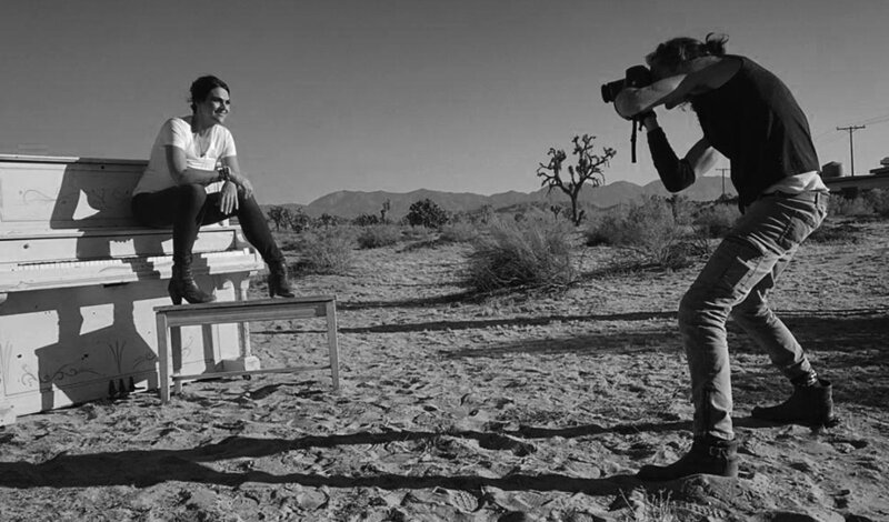 On Location black and white Photo Leslie Cours Mather sitting on piano in desert while photo is being taken Mark Maryanovich photography Lake Los Angeles