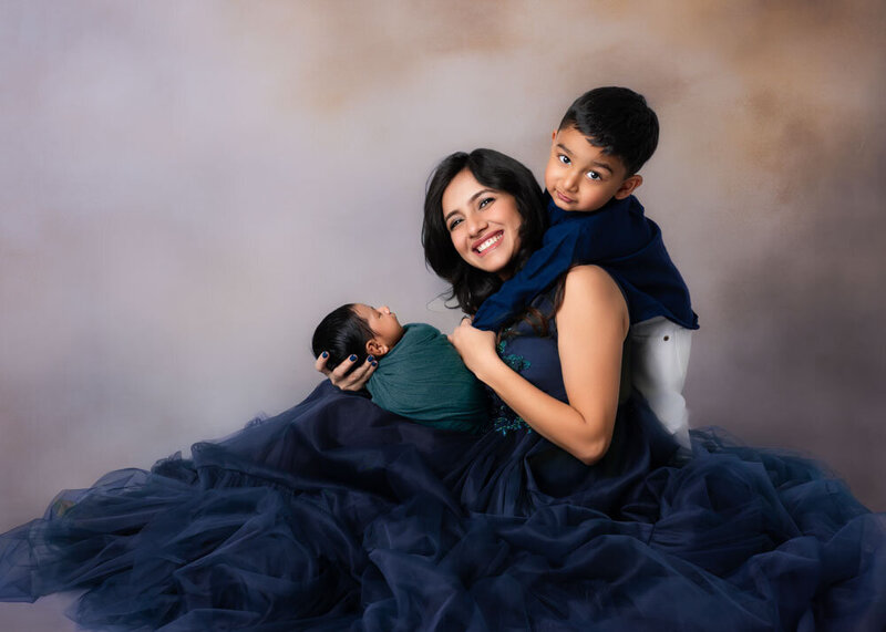 mother-sibling-hugging-newborn-dark-fabric