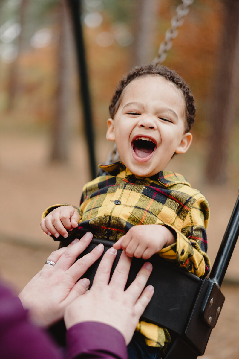 Little boy laughing hard while being pushed on a swing by his dad.