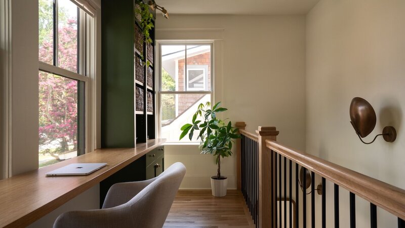Upstairs hallway nook with built-in wooden desk and bold green bookshelf unit, bright natural light from two large windows, maximizing unused space.