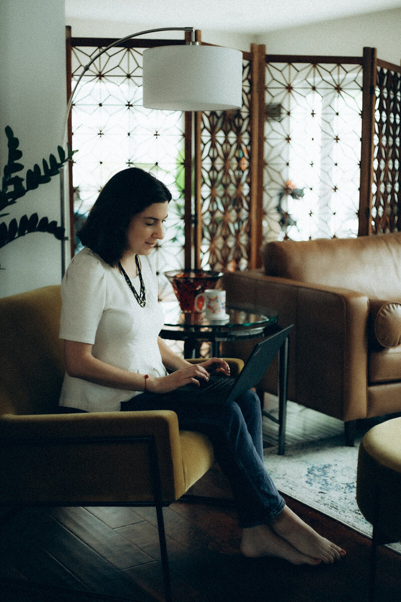 Andrea Shah sitting in a yellow chair working on a laptop