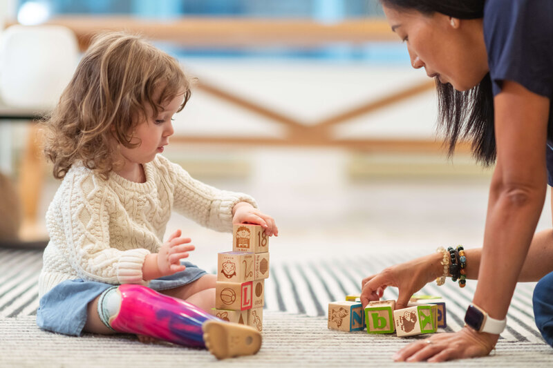 child playing with blocks on the ground. Teacher helping