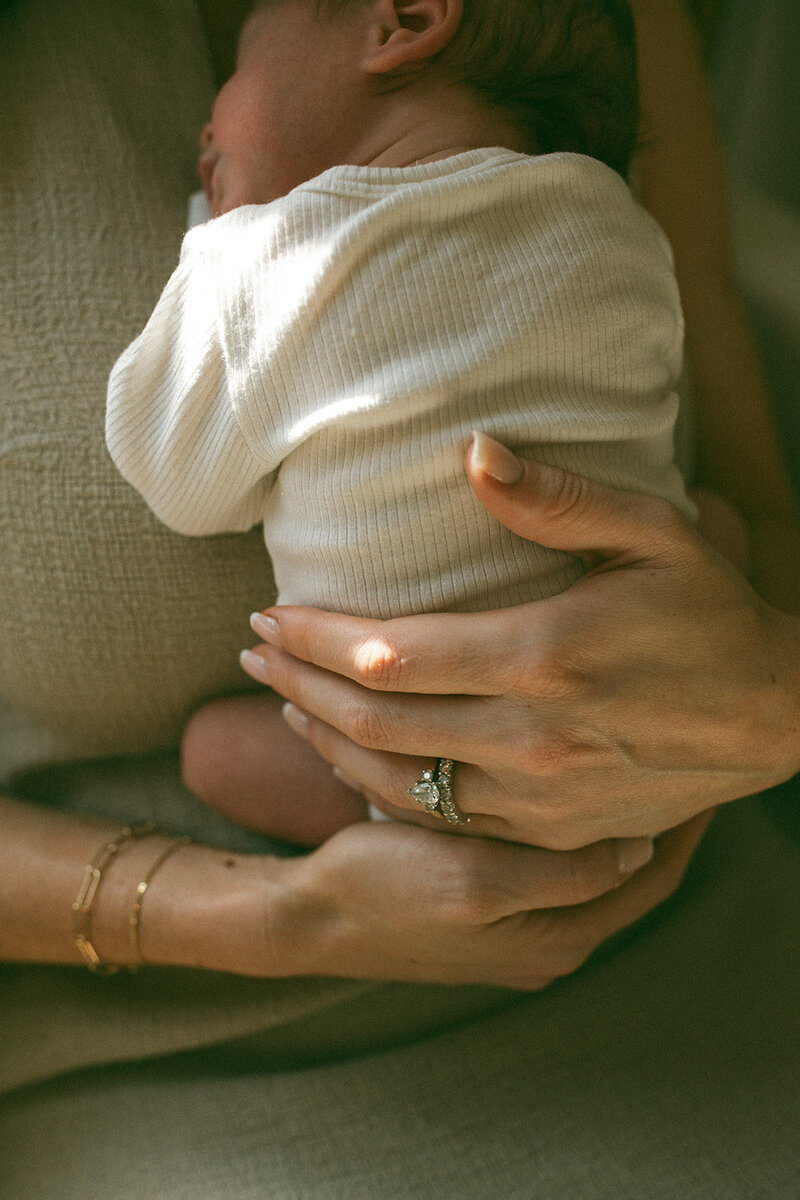 Close-up of a mother’s hands cradling her newborn baby, captured during a candid in-home family photography session