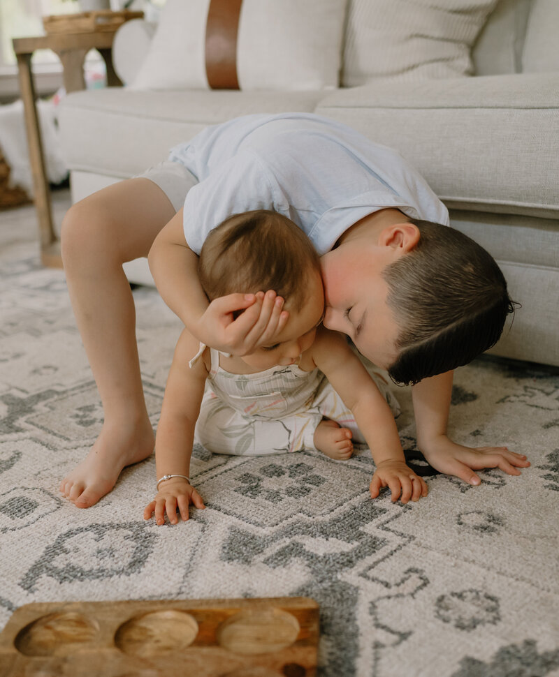 Boy kissing his baby sister in the floor of their Boston area home.