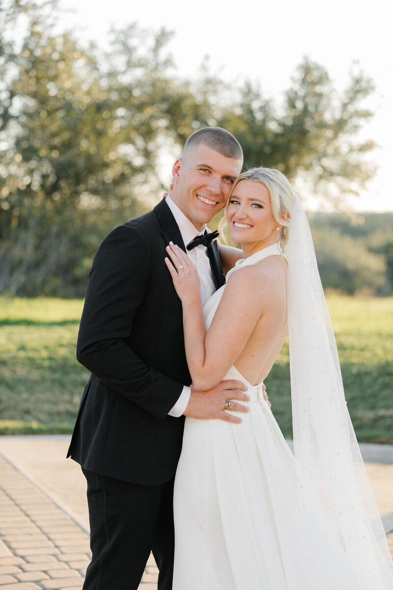 Bride and groom embracing and smiling during sunset portraits in the Texas Hill Country, planned by an Austin wedding planner with heart.