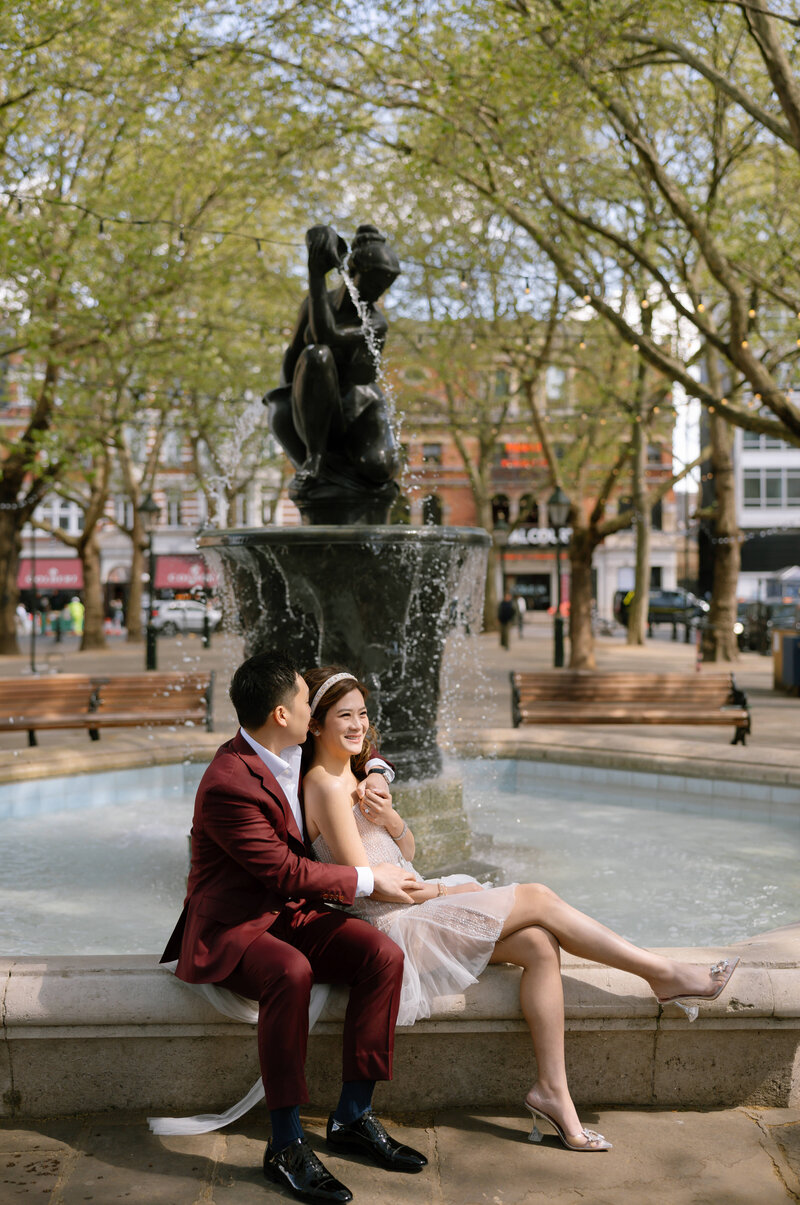 bride and groom sat on fountain in Sloane Square in London