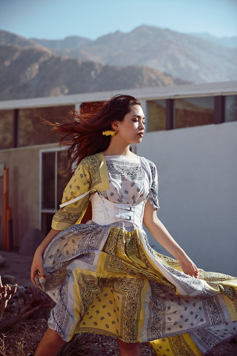 Fashion-forward high school senior in a bold patterned yellow and gray dress twirling in front of a modern home in Palm Springs, California, with scenic desert mountains in the background – editorial-style senior portrait from a styled photography workshop