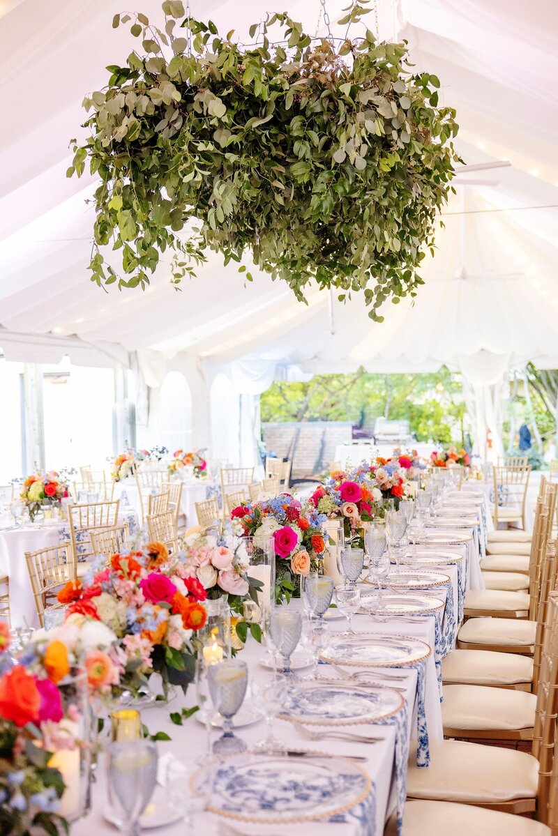 Vibrant and colorful floral arrangements laid on reception tables under an outdoor event tent