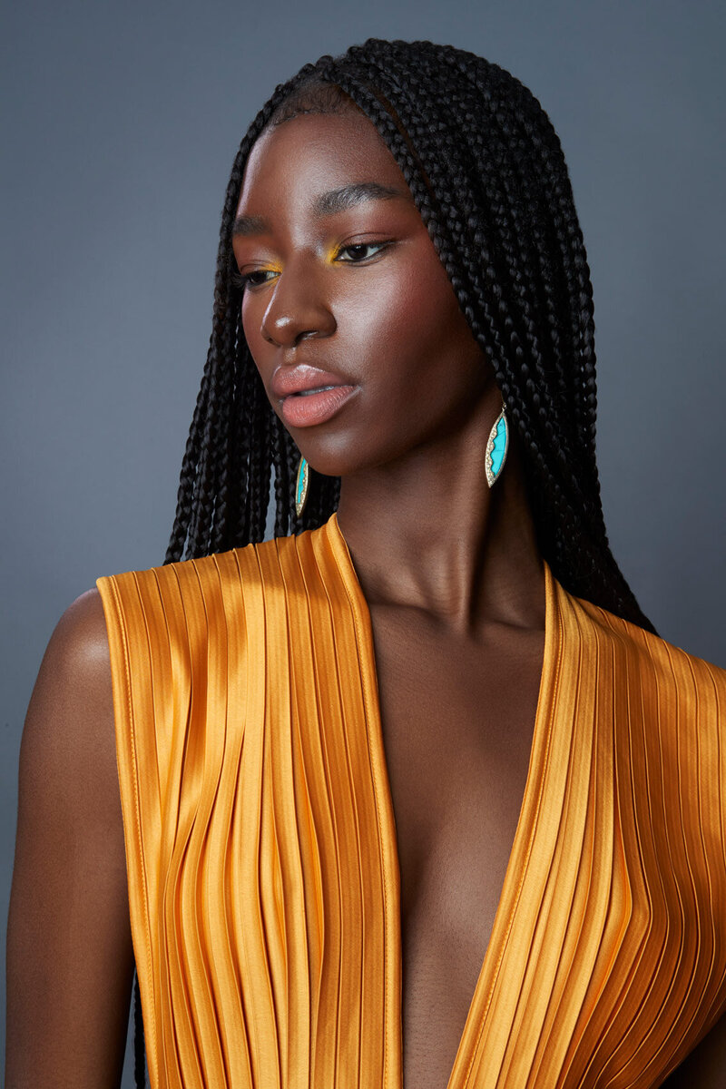 Tracy Masa in a striking studio portrait, wearing a bright yellow outfit with natural curls, shot by Ylva Erevall.