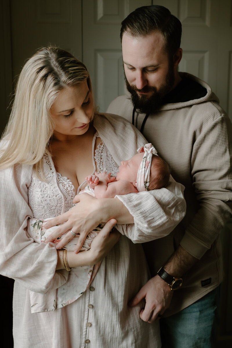 Mom holding baby wearing pink while dad is standing next to them in tan and jeans in baby nursery in Severn, Maryland photographed by Bethany Simms Photography