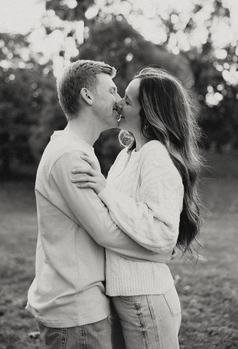 A young couple sharing an embrace and kissing in a field at Loose Park by the Plaza in Kansas City, Missouri. Black and white vintage edit