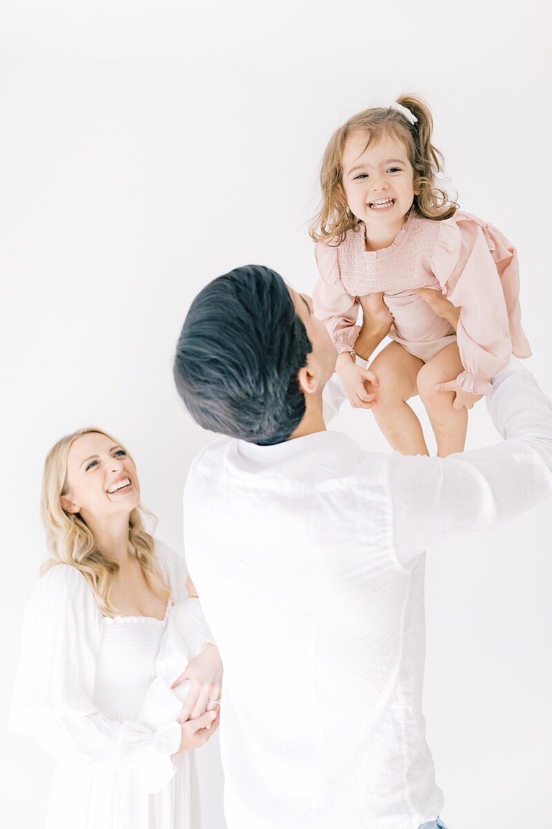 A Charlotte Newborn Photographer captures the special moment of a mom and dad joyfully holding their baby girl in the air.
