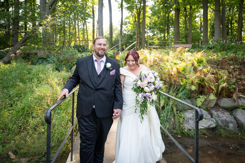 bride and groom walking together along small bridge in park