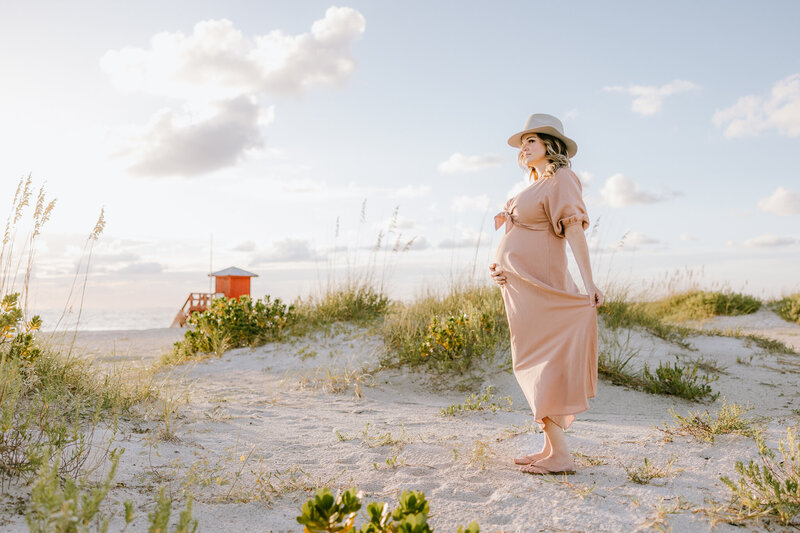 Pregnant woman in pink dress on the beach captured by Tampa maternity photographer.