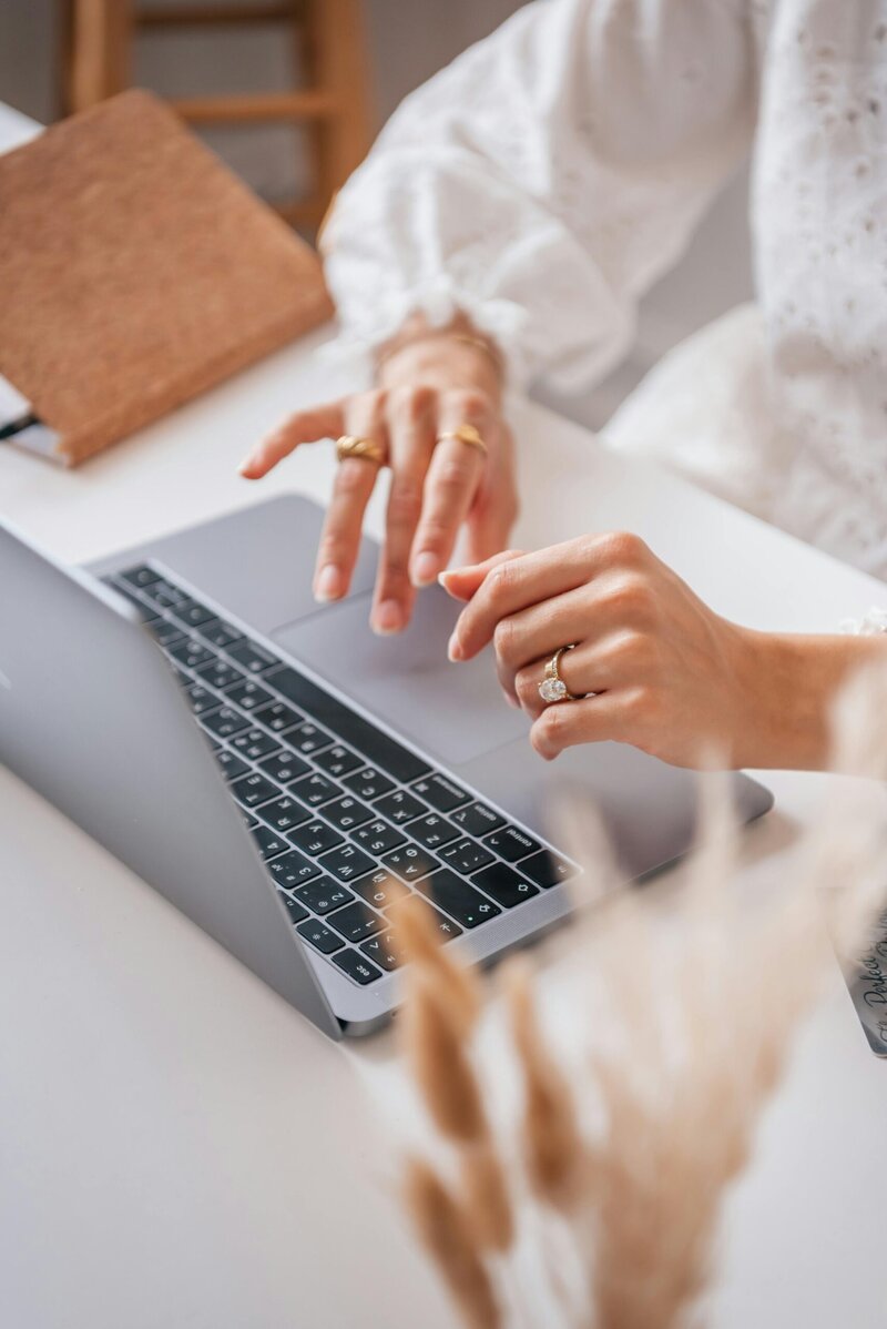 MacBook on a white table with peach-colored flowers in a gold watering can, creating a calming and professional workspace for wellness professionals.