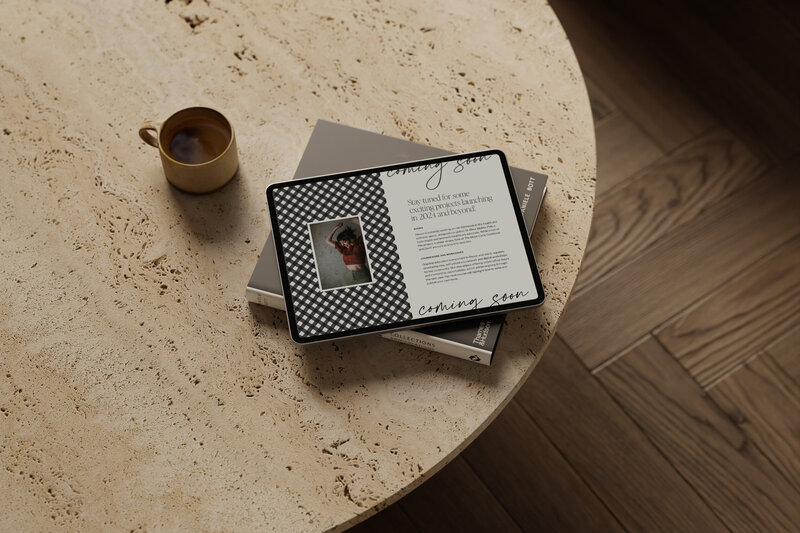 Tablet displaying a 'Coming Soon' webpage design with a checkered design and project announcement, resting on a textured stone table with books.