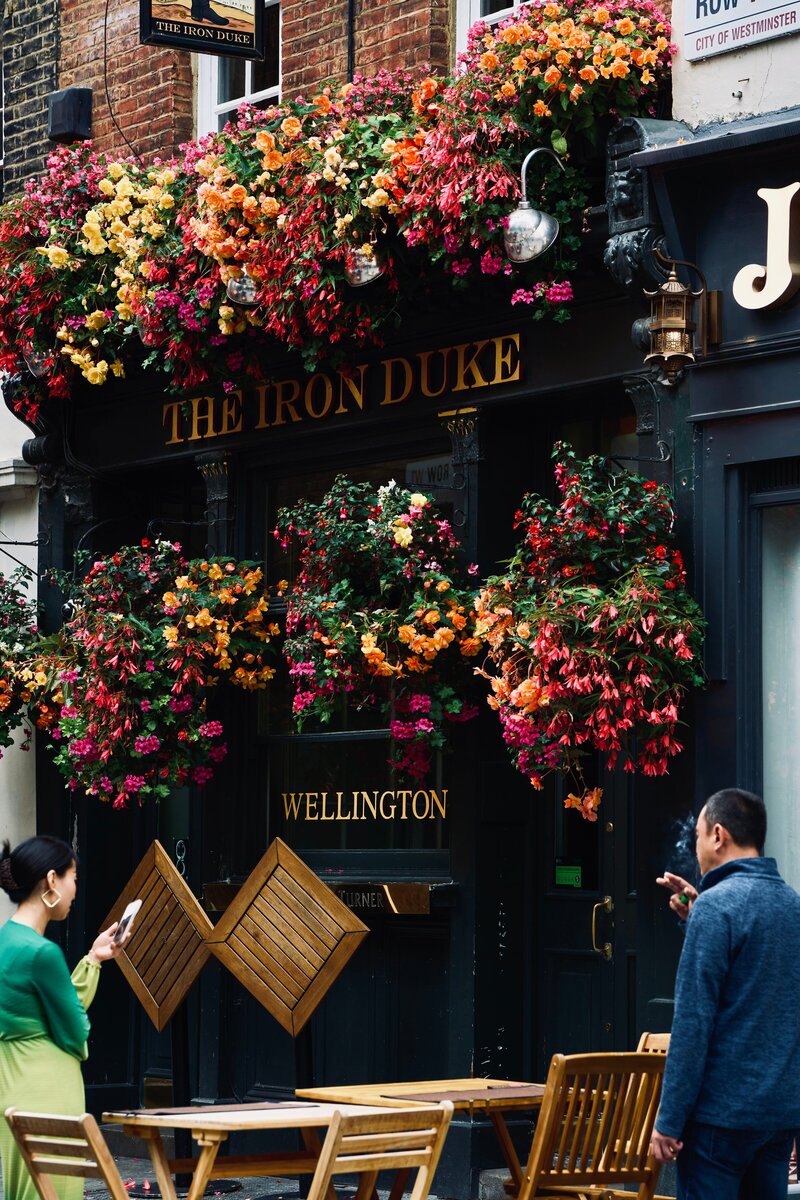 London's Iron Duke Pub sign with colorful flowers overflowing around it with people standing out in front of the pub