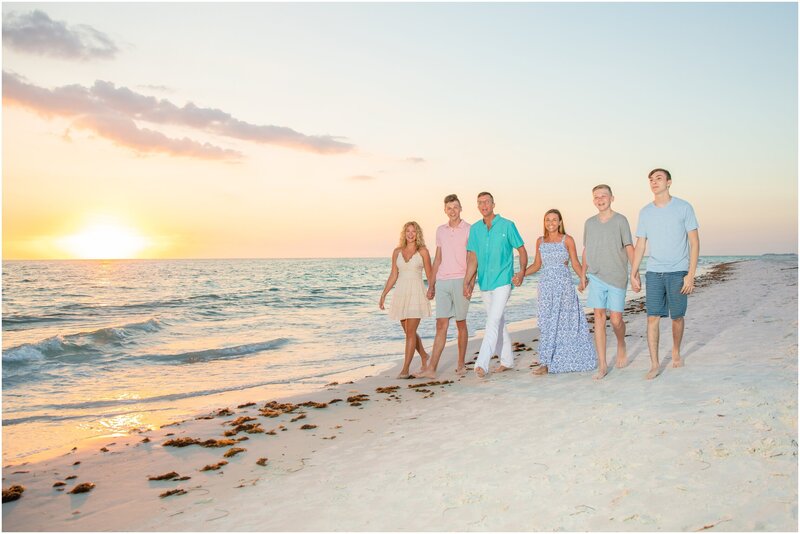 A family holding hands walking on Coquina Beach at sunset