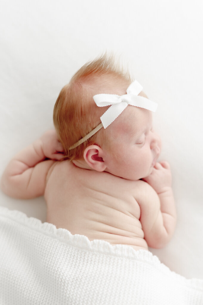 newborn baby wearing a bow and scrunched up with belly rolls in focus