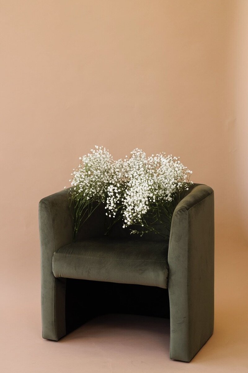 green velvet chair with bunches of baby's breath tied to the arms