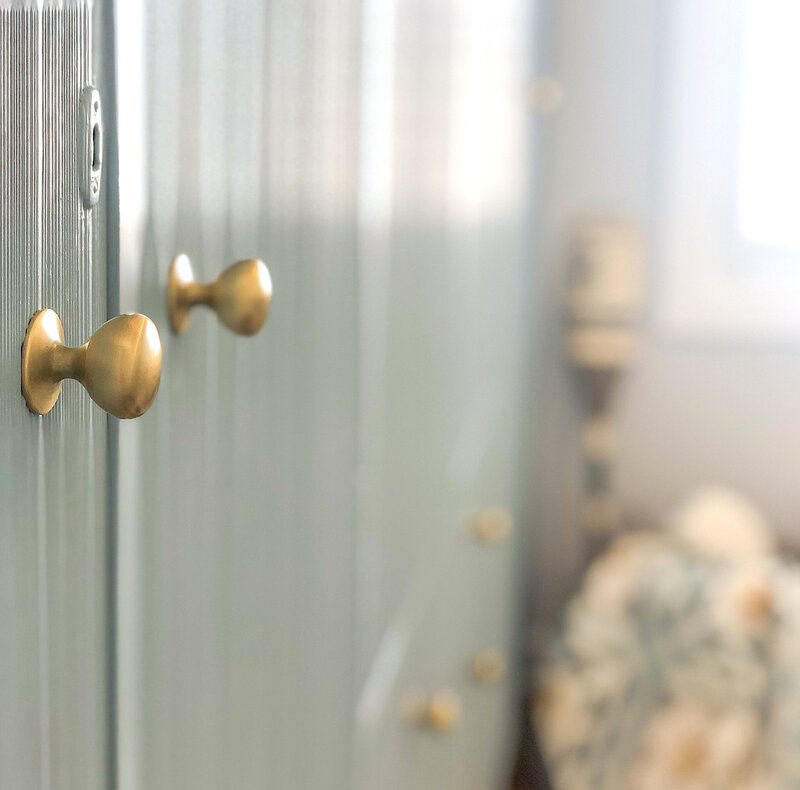 Close-up of brass knobs on a light blue textured cabinet, showcasing the expertise of Newcastle Interior Designer, with soft focus on a cozy, patterned pillow in the background.