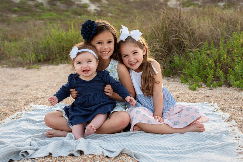 Sisters dressed in blues, pink, and white sit on blanket at Guana Reserve Beach in Ponte Vedra, FL.