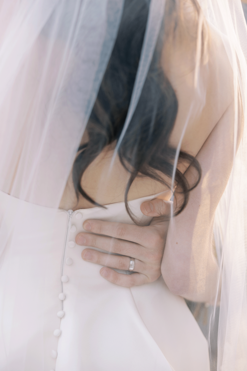 Close-up of the groom's hand gently holding the bride's waist under her veil, showcasing the intimacy of their Blackstone Hotel wedding, planned by Chicago wedding planner Savoir Fête.