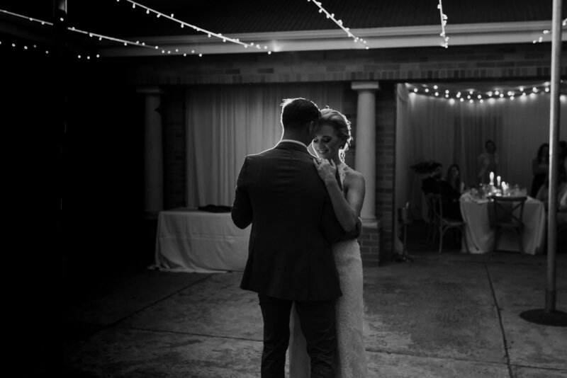 A bride and groom share their first dance at the wedding reception , they are lit from behind and fairy are glowing , it is a romantic whimsical moment