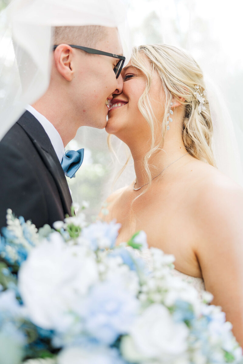 A man holds his fiancee as she smiles at the camera and he presses his forehead up against hers.