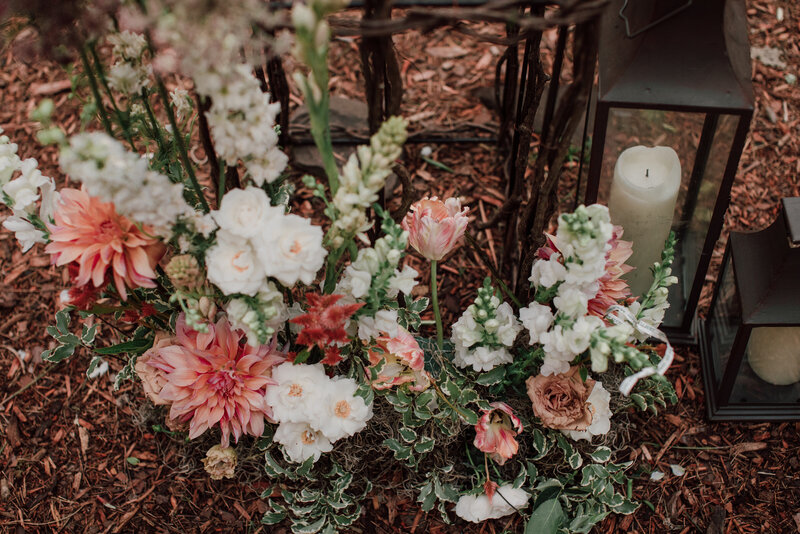 Peach copper and ivory wedding ceremony aisle arrangements with bronze lanterns rest on the forest floor