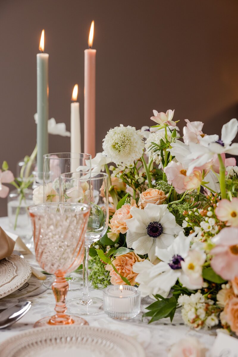 Intimate wedding table setup with pastel floral arrangements, taper candles in soft hues, and vintage-inspired glassware.