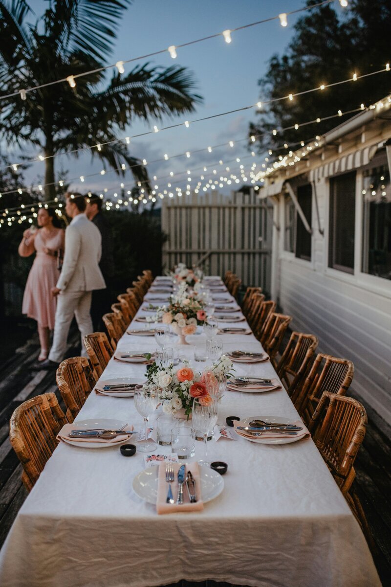 Table dressée en extérieur à la nuit tombée et lumières suspendues. Décor pour crée pour l'organisation de baptême.