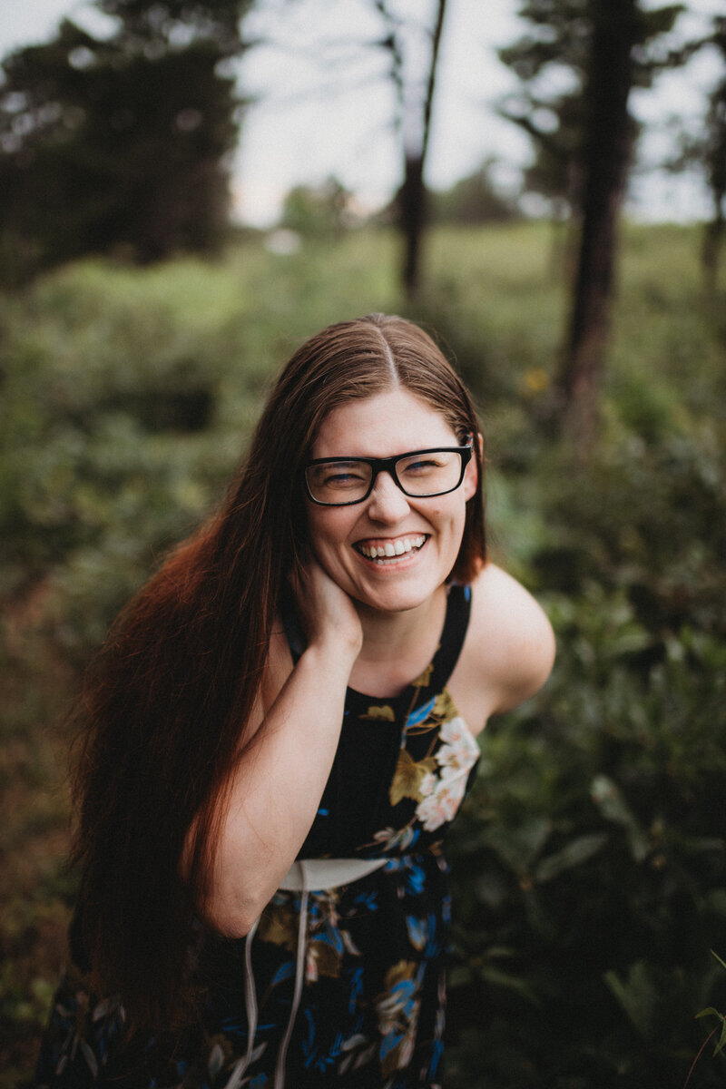 Melissa Marino, photographer, wears glasses and a floral dress while laughing into camera