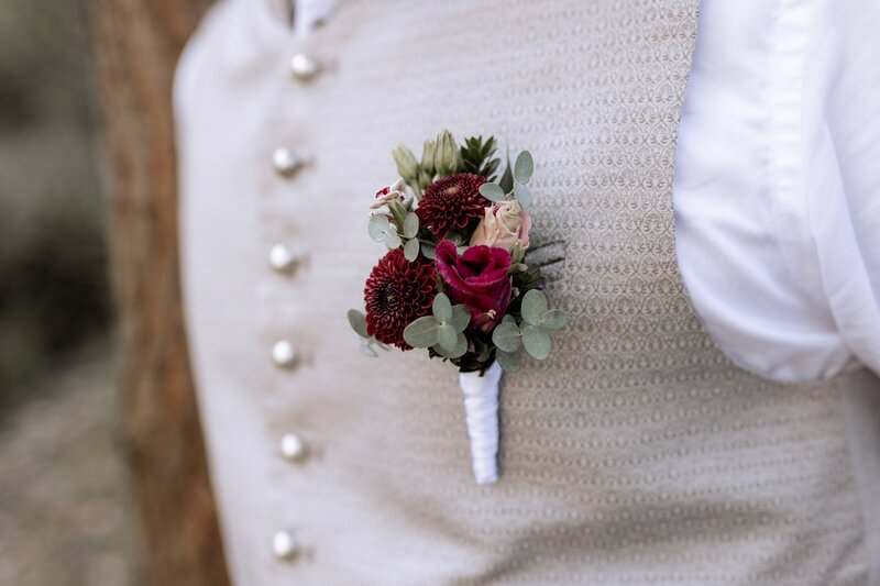 Detailfoto von Anstecker des Braeutigams mit roten Blumen
