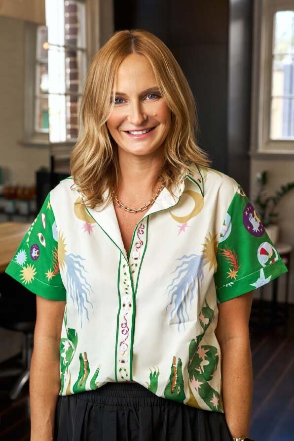 Katy Reeve wearing a colourful patterned shirt with celestial designs, posing in a well-lit salon interior.