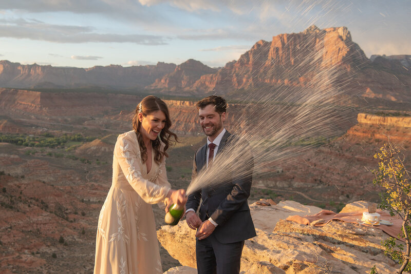 couple popping Champagne after they shared private vows on Zion National Park cliff 