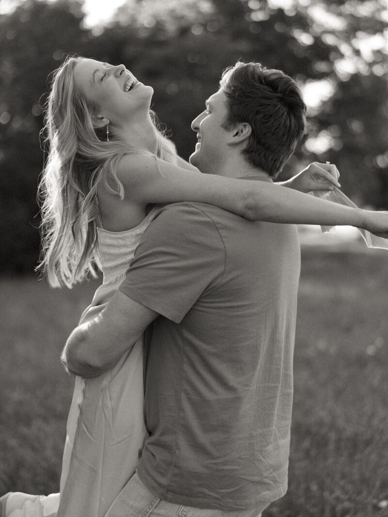 Black and white photo of man picking up woman as she laughs