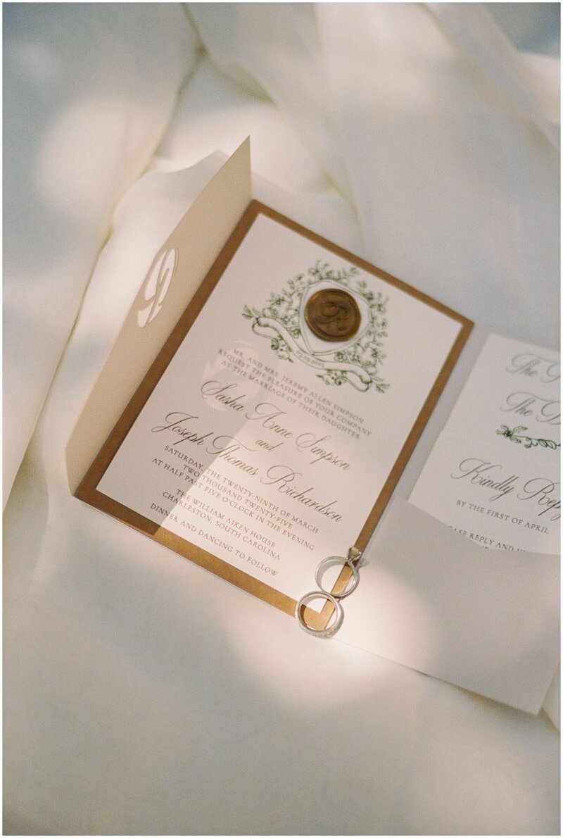 A bride's rings lay on her invitation on a white bed