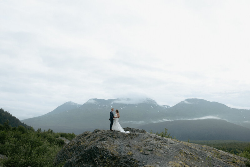A couple taking in mountain views while standing on a rock.