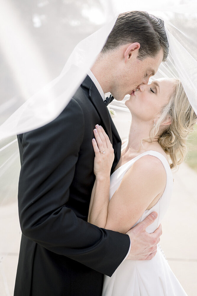 bride and groom kissing while wrapped in the bride's veil