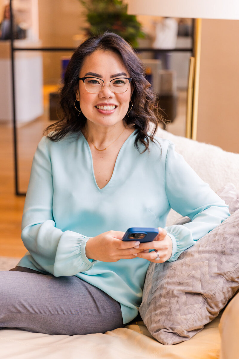 woman sitting on sofa wearing light blue top  working on her phone personal branding session laure branding photographer atlanta brand photographer