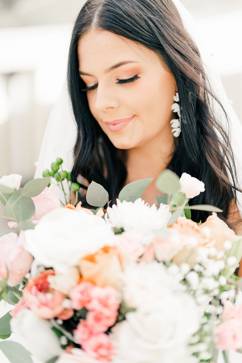 natural makeup on a bride with dark hair, white flower earrings, a pearl veil, and a bouquet with white and greeen