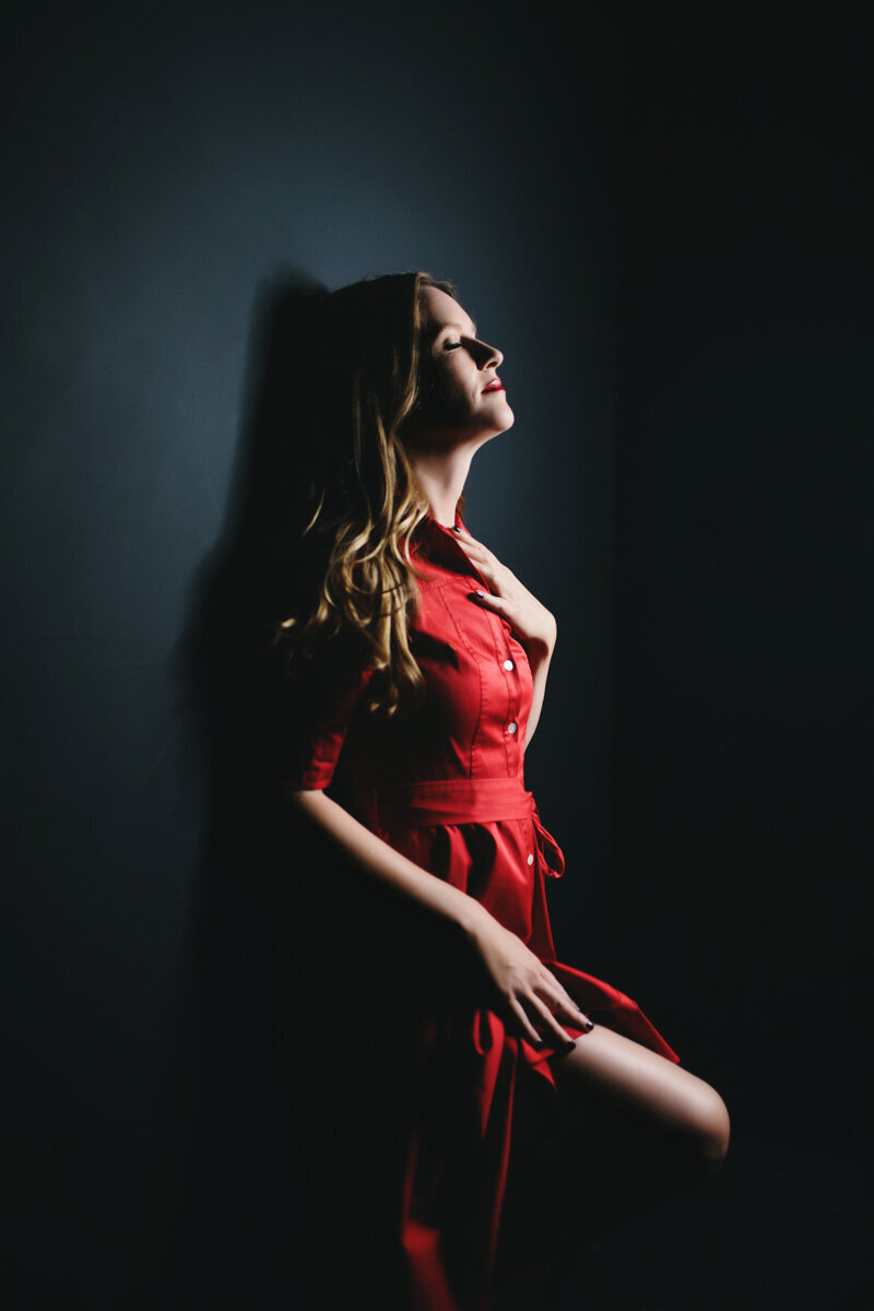 woman wearing red dress leaning against black wall