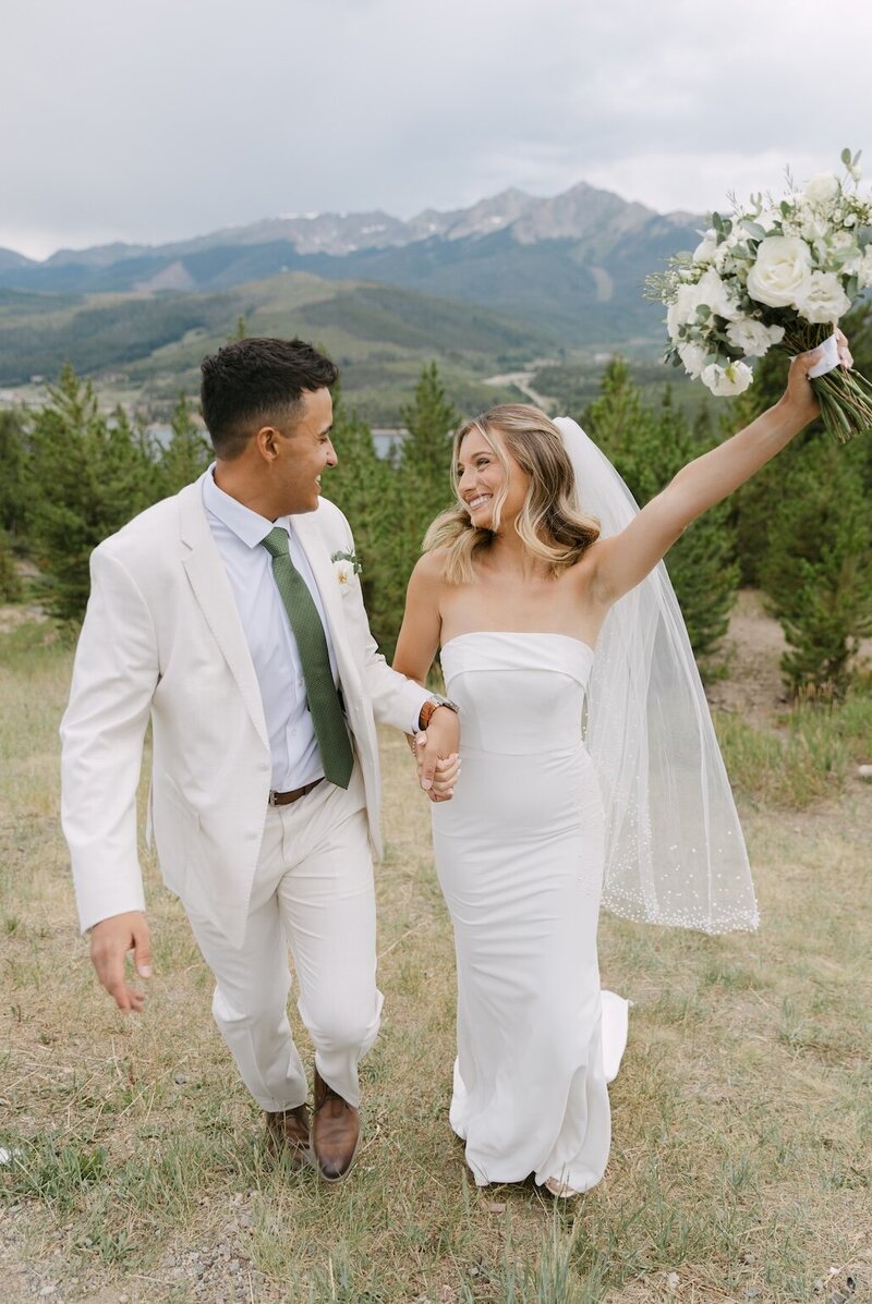 Bride and groom walking through a Colorado mountain meadow with bouquet raised after their Sapphire Point Overlook wedding ceremony
